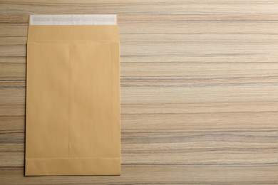 Photo of Kraft paper envelope on wooden background, top view. Space for text