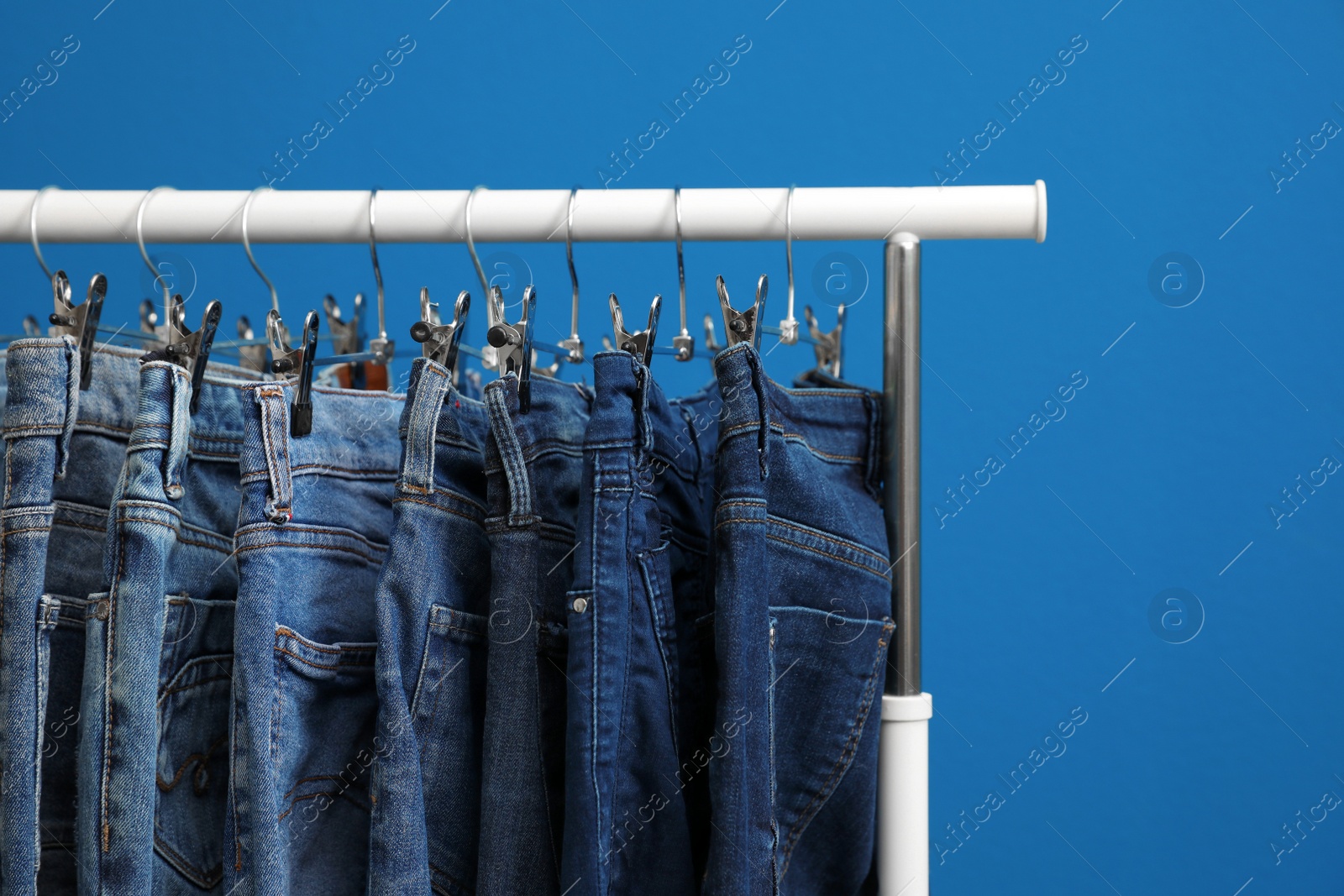 Photo of Rack with stylish jeans on blue background, closeup