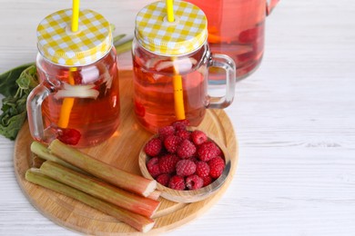 Photo of Tasty rhubarb cocktail with raspberry and stalks on white wooden table. Space for text