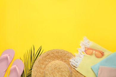 Photo of Beach towel, flip flops, straw hat and sunglasses on yellow background, flat lay. Space for text