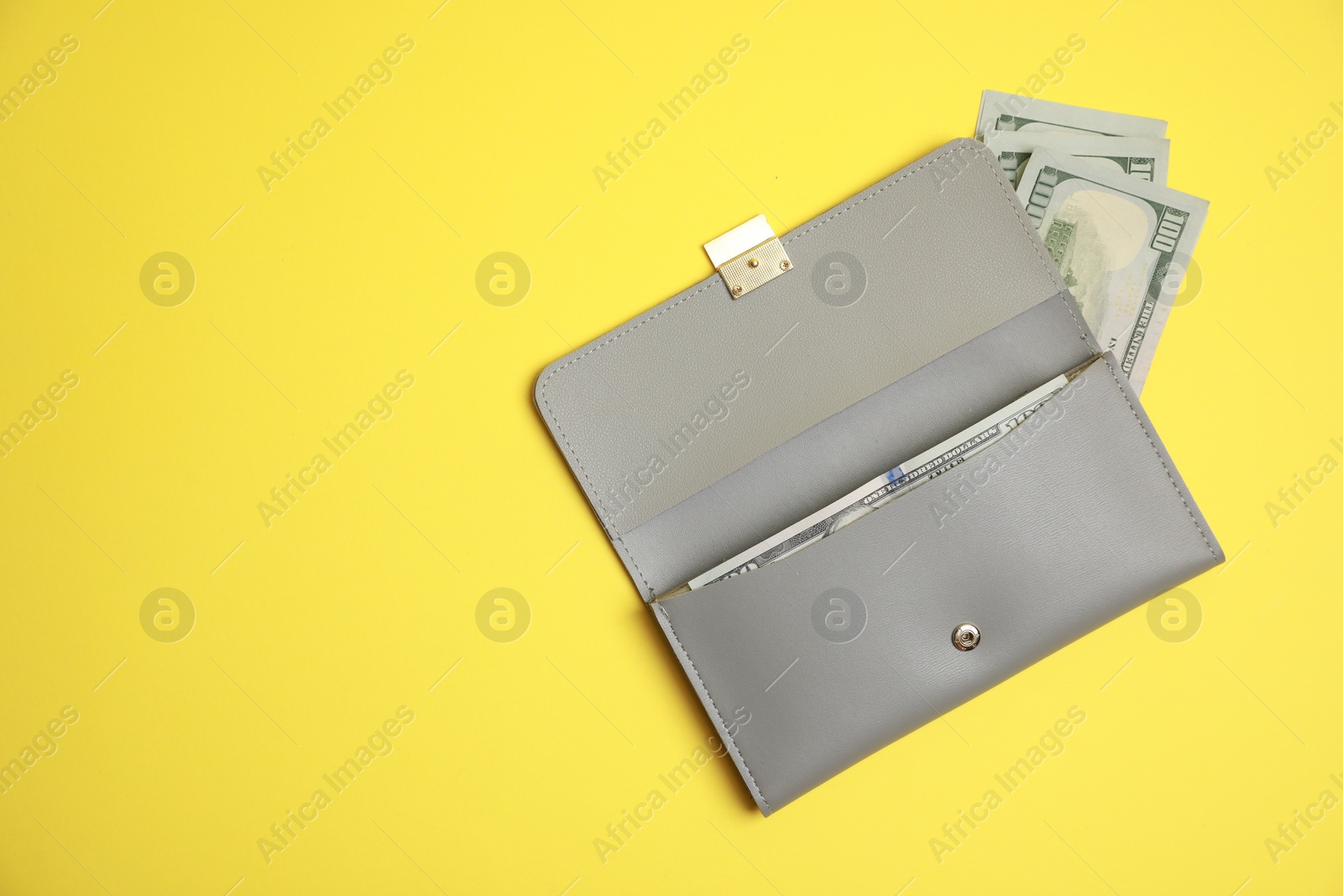 Photo of Stylish light grey leather purse with dollar banknotes on yellow background, top view. Space for text