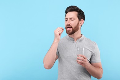 Photo of Handsome man with glass of water taking pill on light blue background, space for text