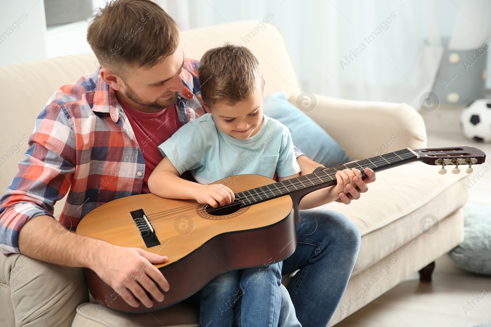 Photo of Father teaching his little son to play guitar at home