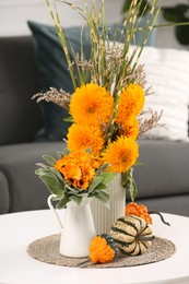 Photo of Beautiful bouquets with bright orange flowers and pumpkins on coffee table indoors. Autumn vibes