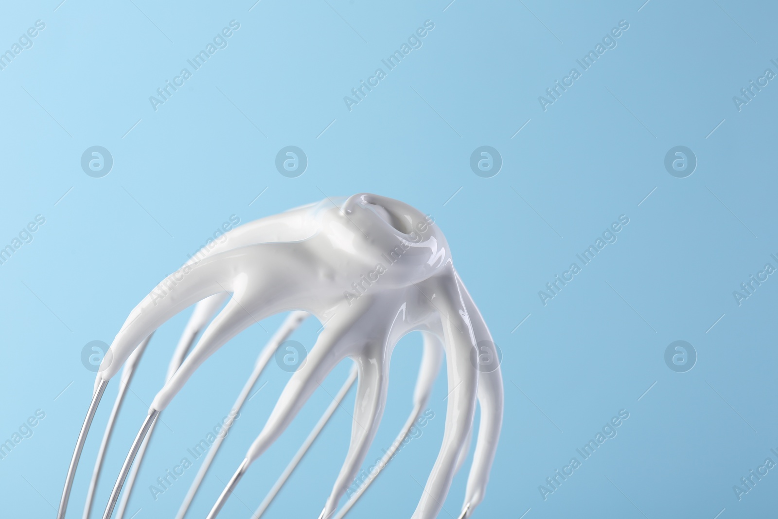 Photo of Whisk with whipped cream on light blue background, closeup. Space for text