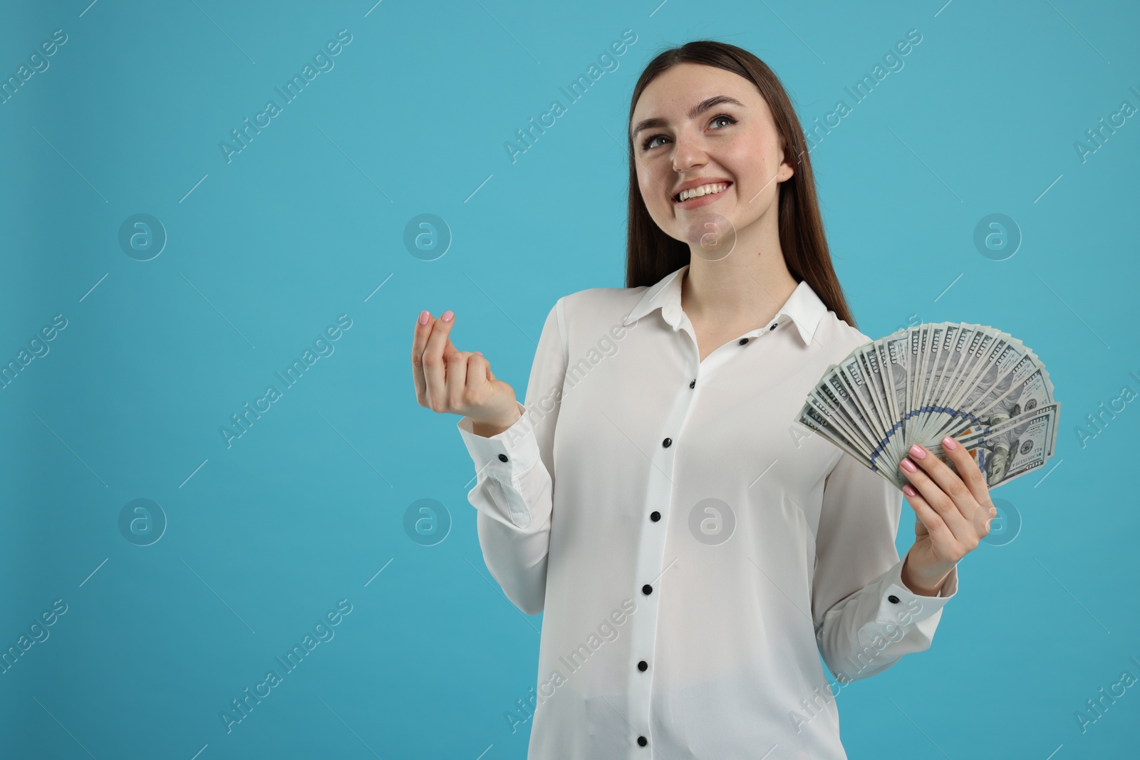 Photo of Happy woman with dollar banknotes showing money gesture on light blue background, space for text