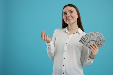 Happy woman with dollar banknotes showing money gesture on light blue background, space for text