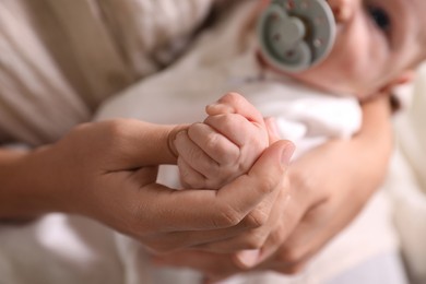 Photo of Mother holding newborn baby indoors, focus on hands