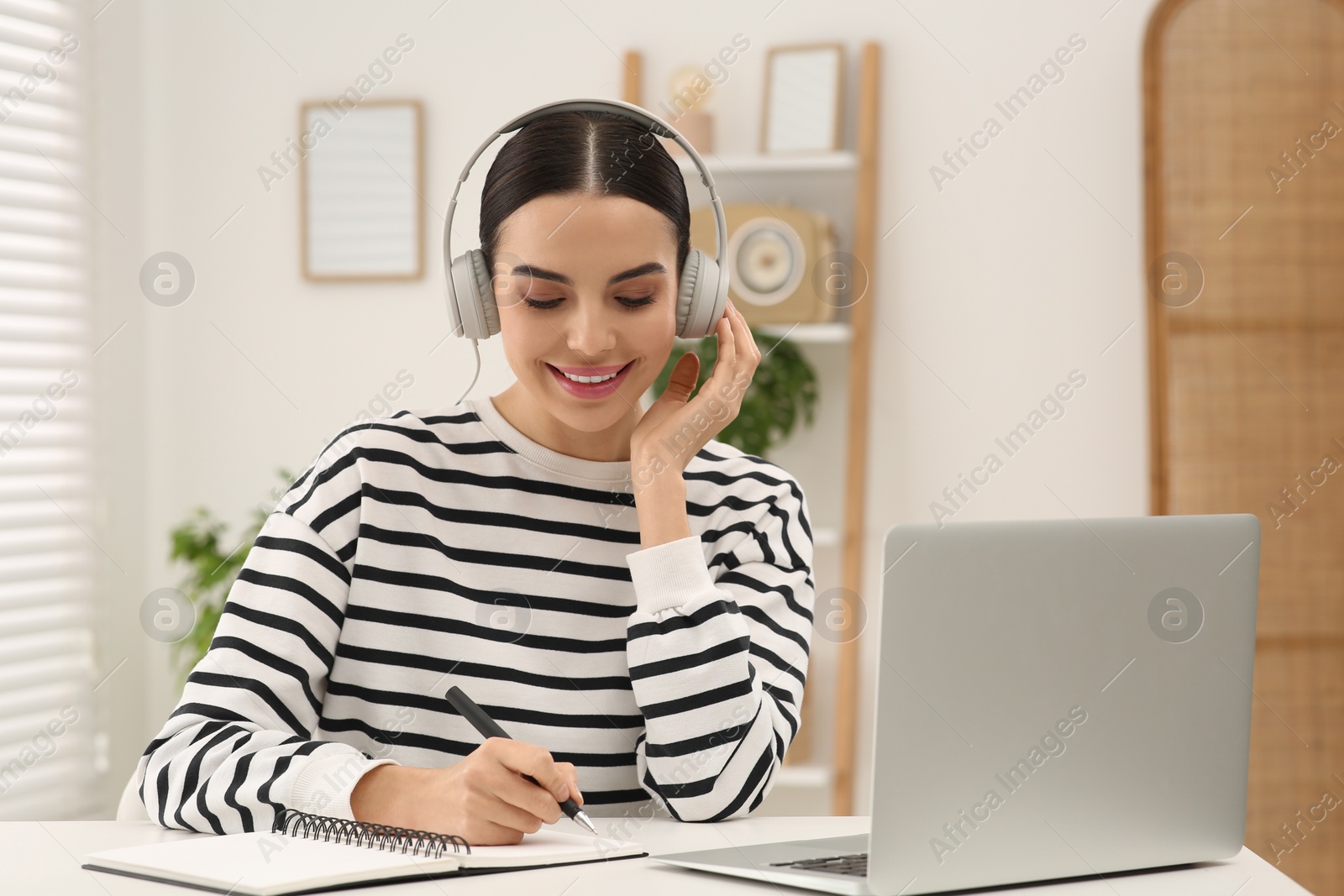 Photo of Online translation course. Student in headphones writing near laptop at home