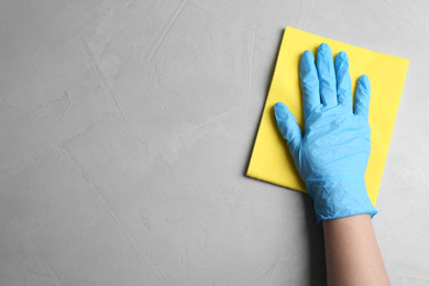 Photo of Woman in gloves wiping grey table with rag, top view. Space for text