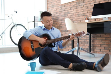 Photo of Happy young businessman playing guitar during break in office. Peaceful moment