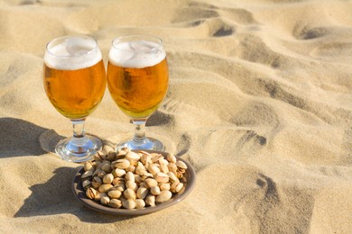 Photo of Glasses of cold beer and pistachios on sandy beach, space for text