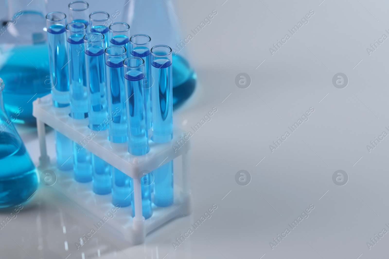 Photo of Laboratory glassware with blue liquid on light background. Space for text