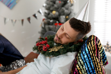 Drunk man with festive cap and wreath sleeping in room after New Year party