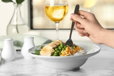 Woman eating tasty boiled rice with meat and vegetables at table, closeup