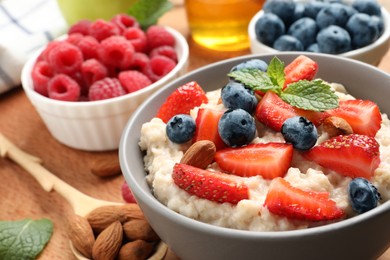 Photo of Tasty oatmeal porridge with berries and almond nuts served on wooden table, closeup