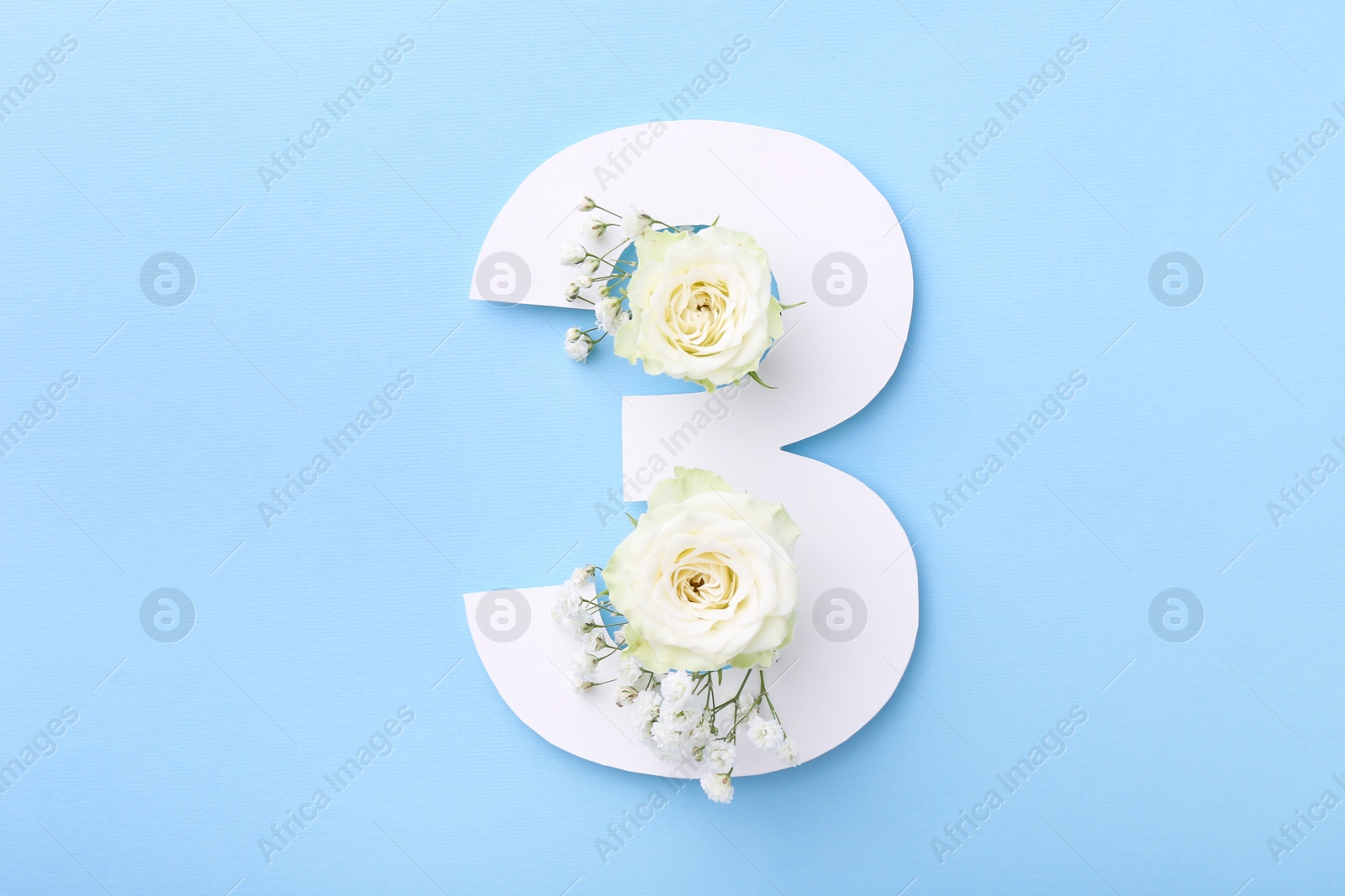 Photo of Paper number 3 and beautiful flowers on light blue background, top view