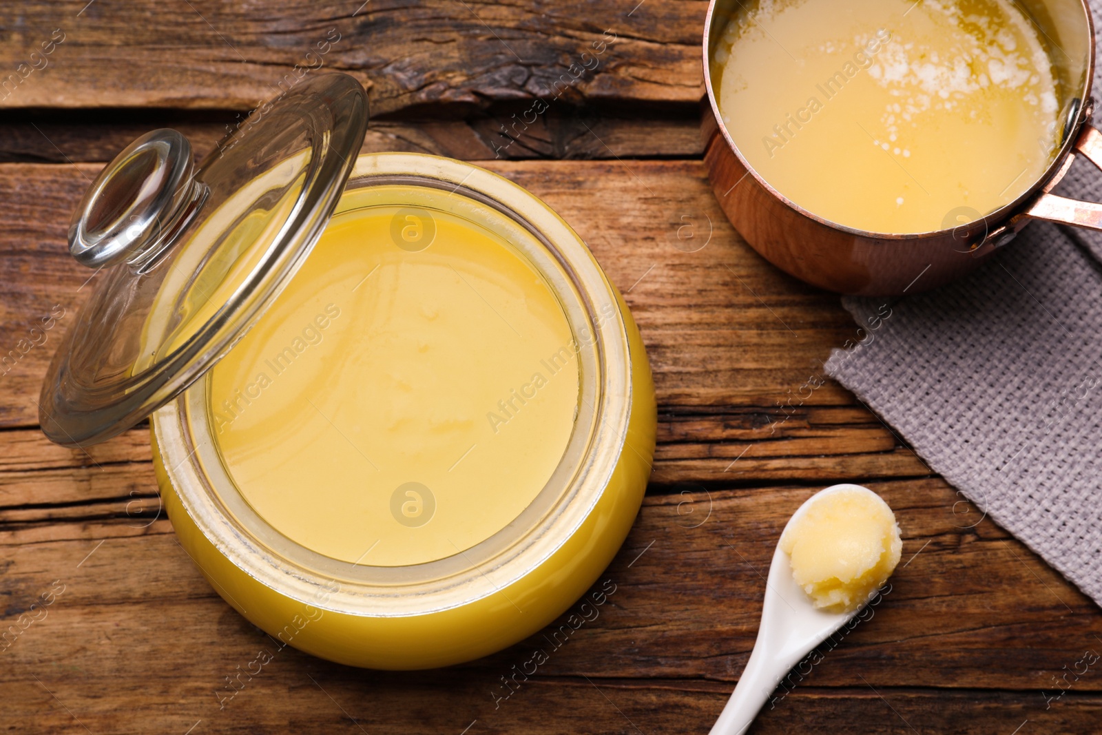 Photo of Ghee butter in dishware on wooden table, flat lay