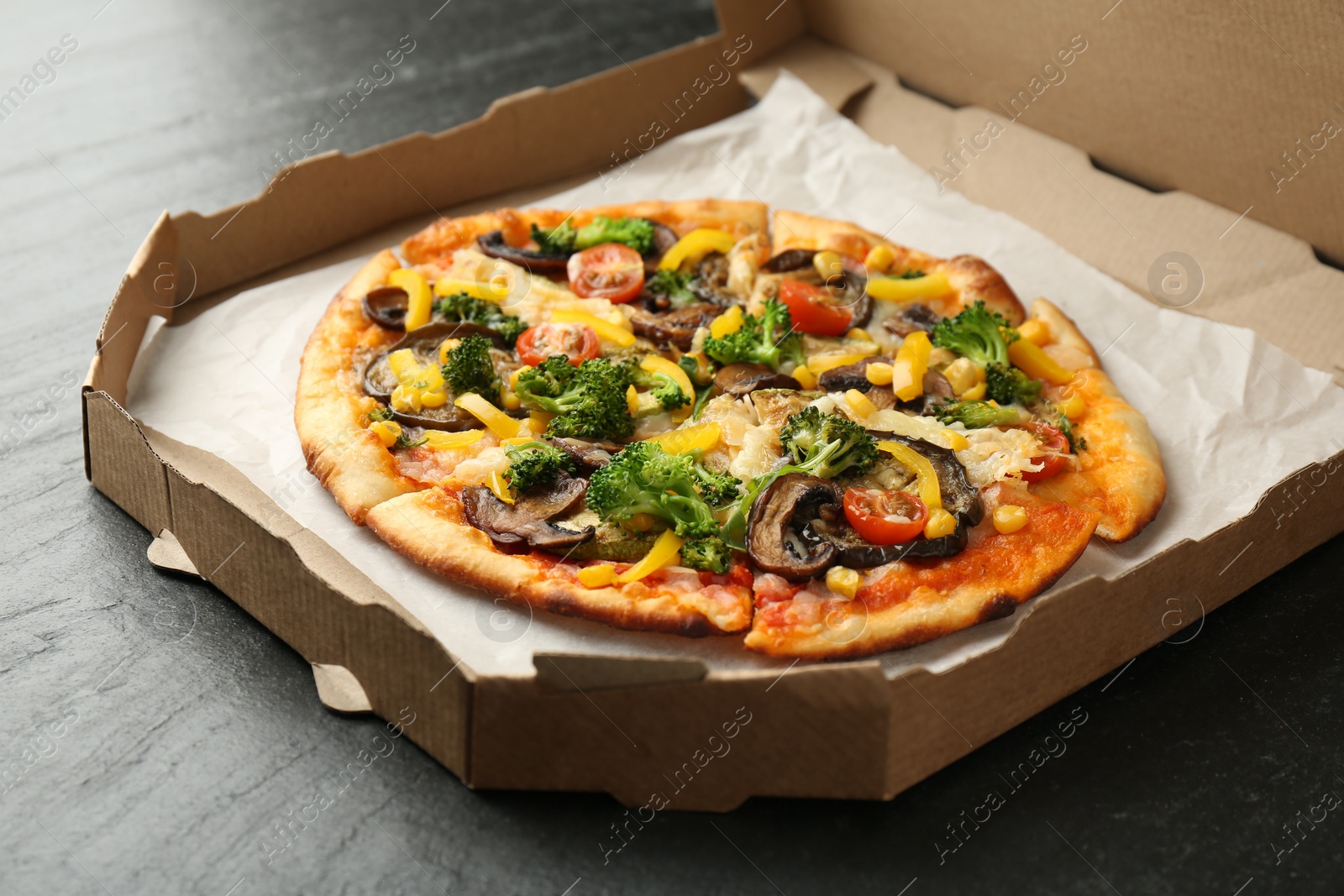 Photo of Delicious vegetarian pizza with mushrooms, cheese and vegetables in box on black table