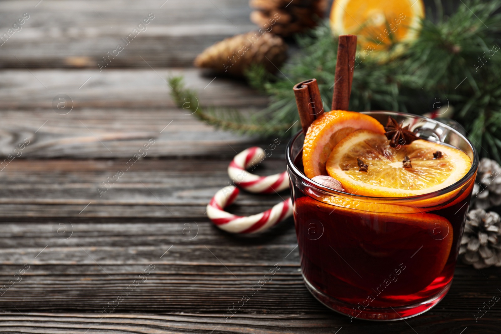 Photo of Glass cup of tasty mulled wine on black wooden table. Space for text