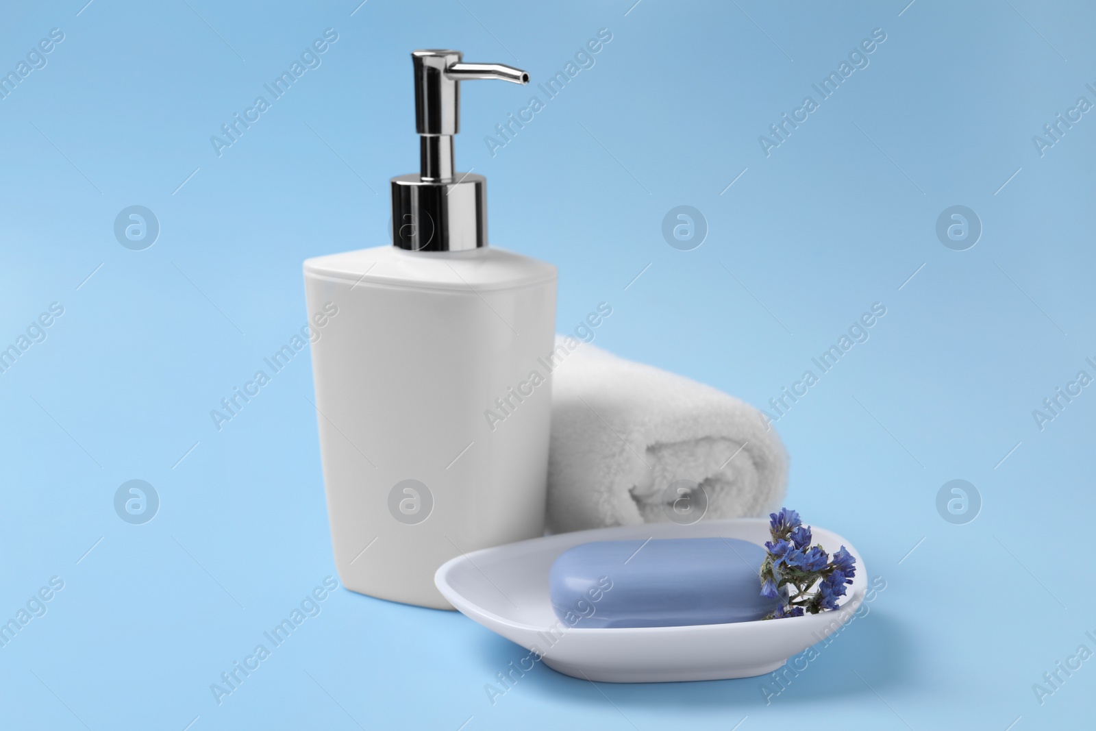 Photo of Soap bar, bottle dispenser and towel on light blue background