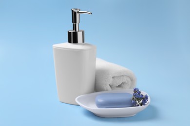 Photo of Soap bar, bottle dispenser and towel on light blue background