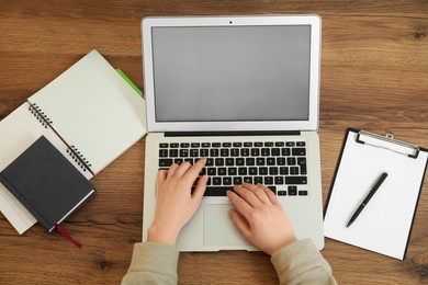 Photo of Woman working on modern laptop at wooden table, top view