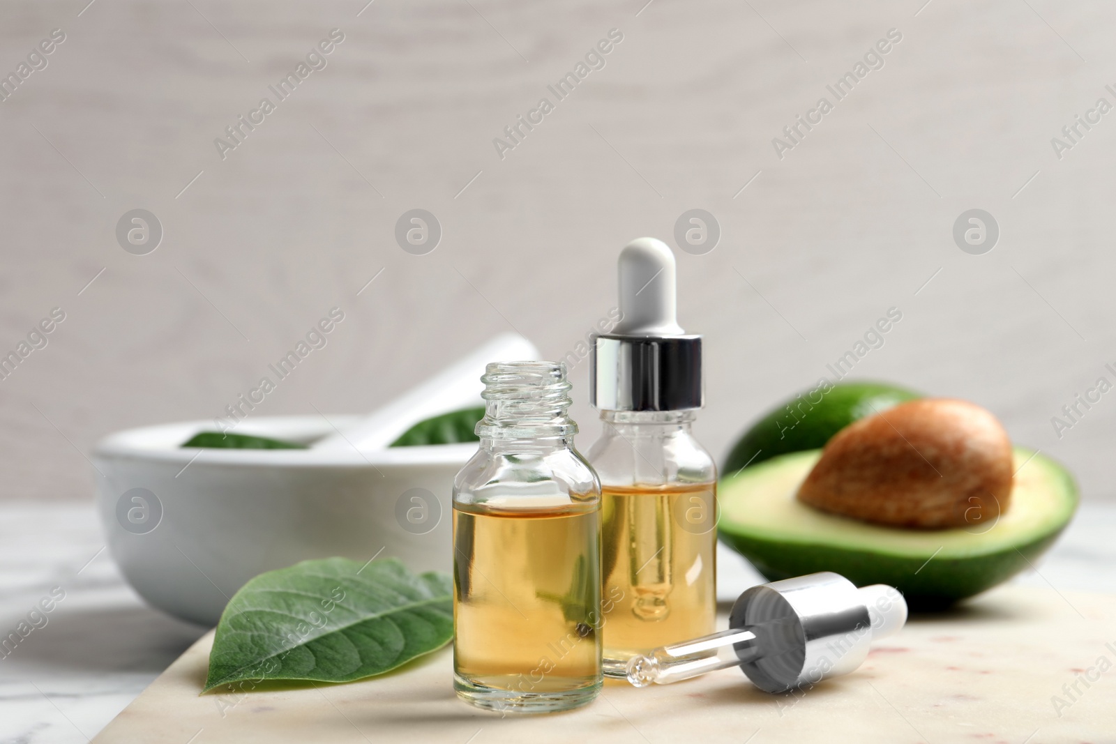Photo of Bottle of essential oil, pipette and fresh avocado on table, closeup