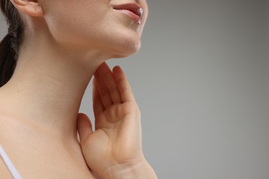 Woman touching her neck on grey background, closeup. Space for text