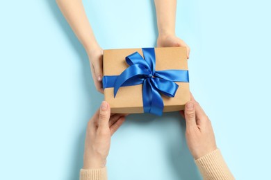 Photo of Mother giving gift box to her child on light blue background, top view