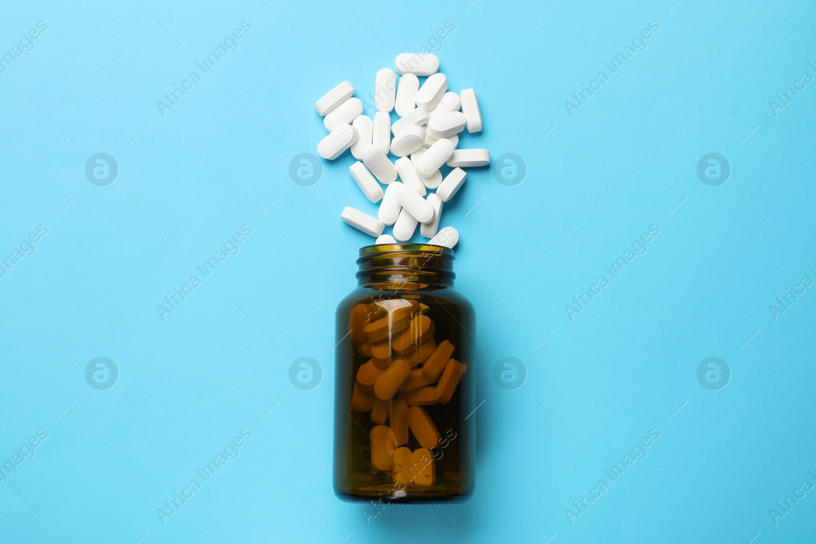 Photo of Bottle and vitamin capsules on light blue background, top view