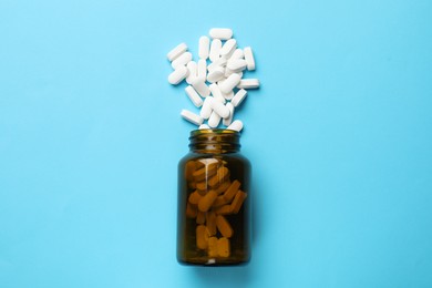 Bottle and vitamin capsules on light blue background, top view