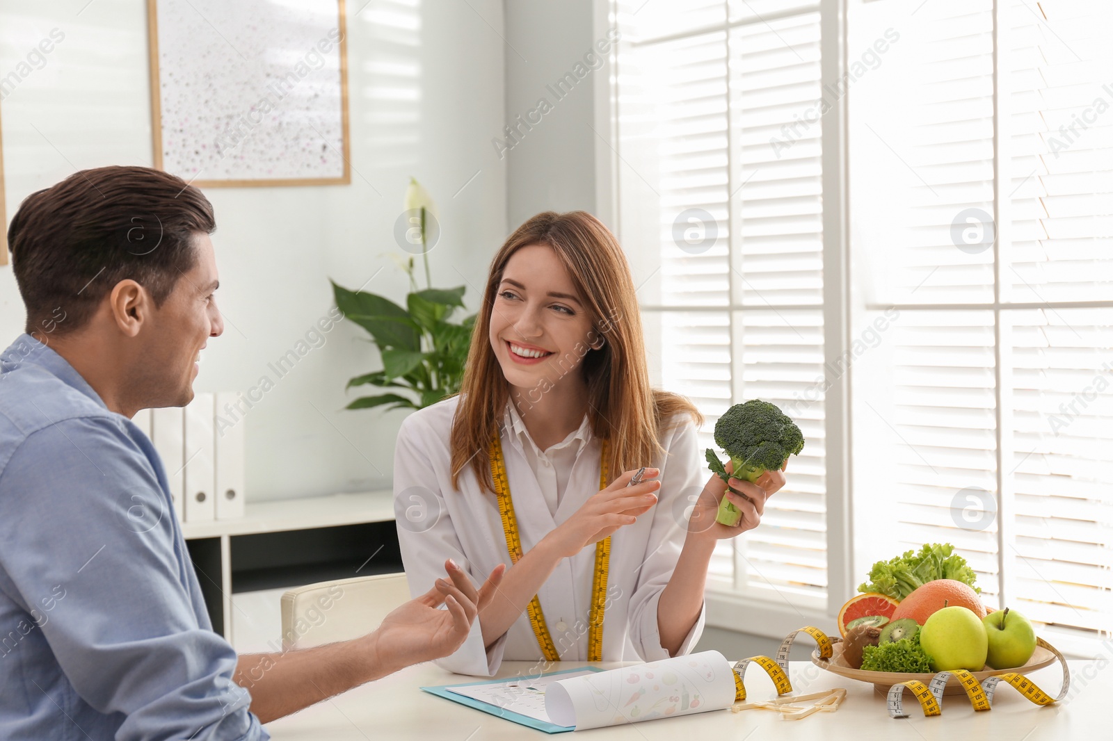 Photo of Young nutritionist consulting patient at table in clinic