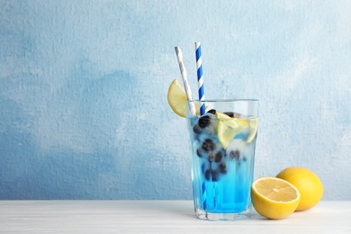 Tasty cocktail with blueberry ice cubes and lemons on table against color background. Space for text