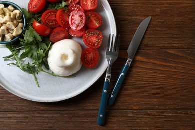 Delicious burrata cheese with tomatoes and arugula served on wooden table, top view