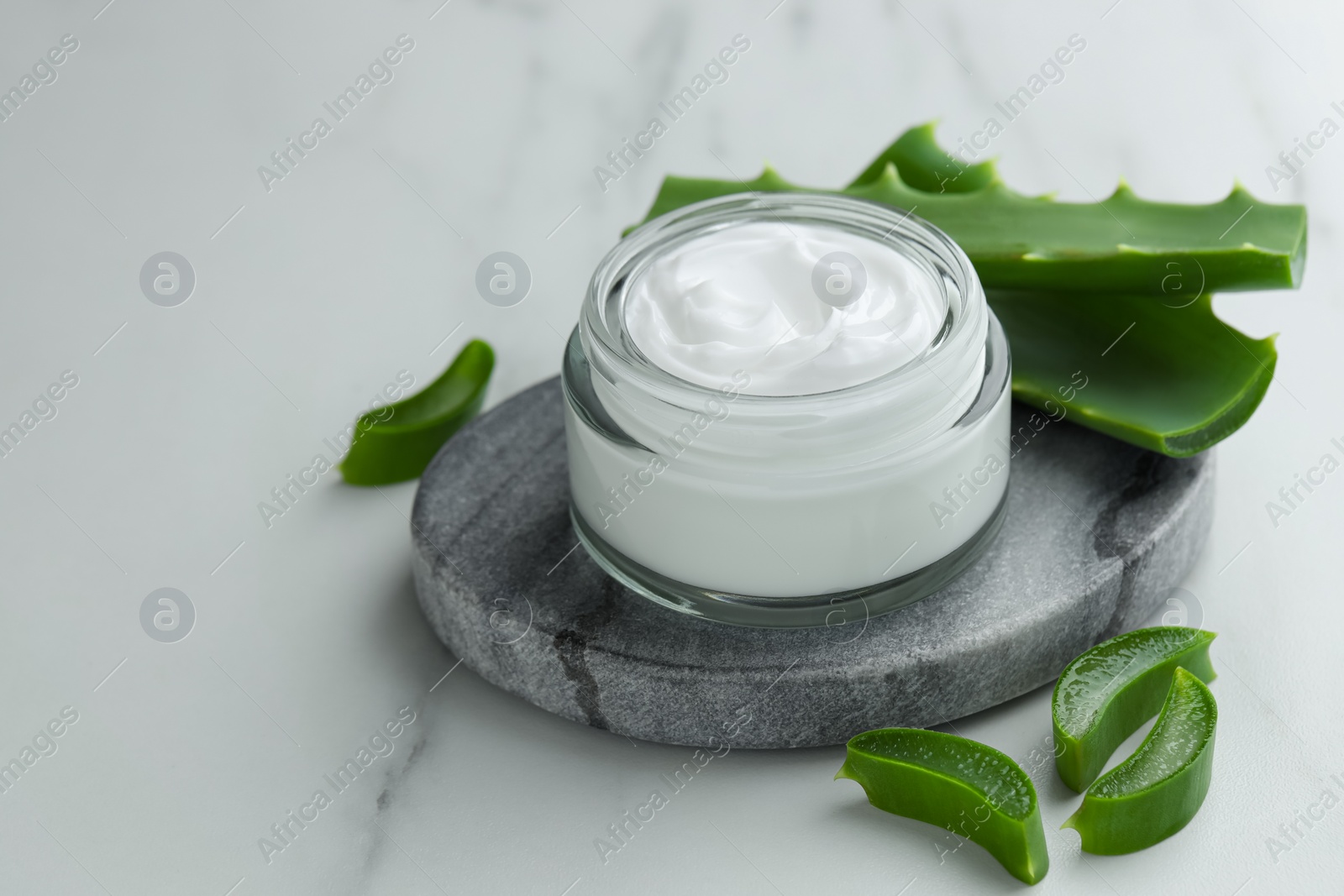 Photo of Jar with cream and cut aloe leaves on white marble table, closeup. Space for text