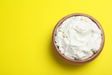 Photo of Bowl of tasty cream cheese on yellow background, top view. Space for text