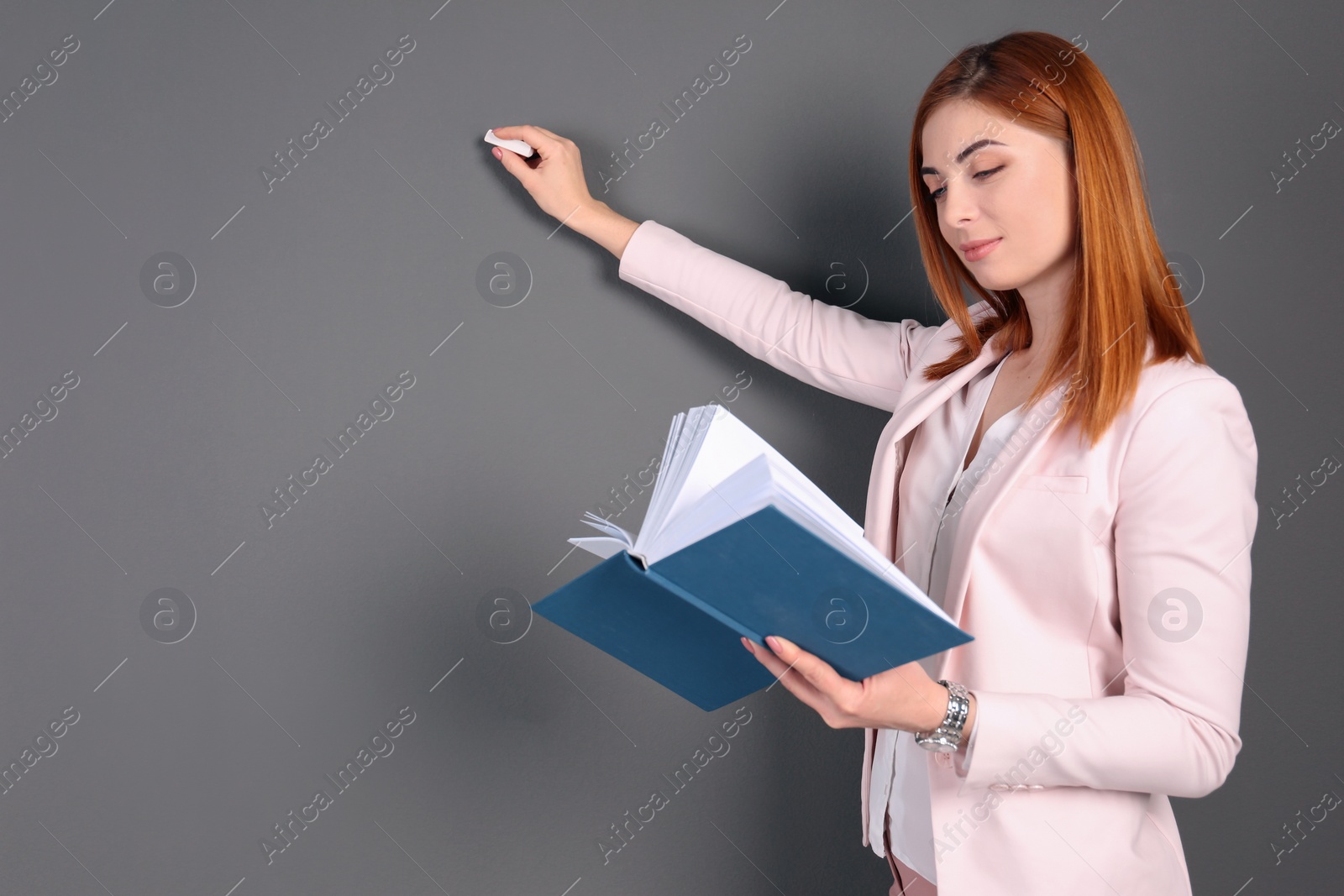 Photo of Beautiful young teacher with book and chalk on grey background