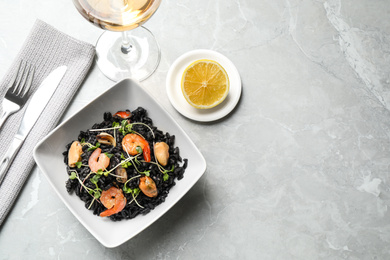 Delicious black risotto with seafood served on light grey marble table. Space for text
