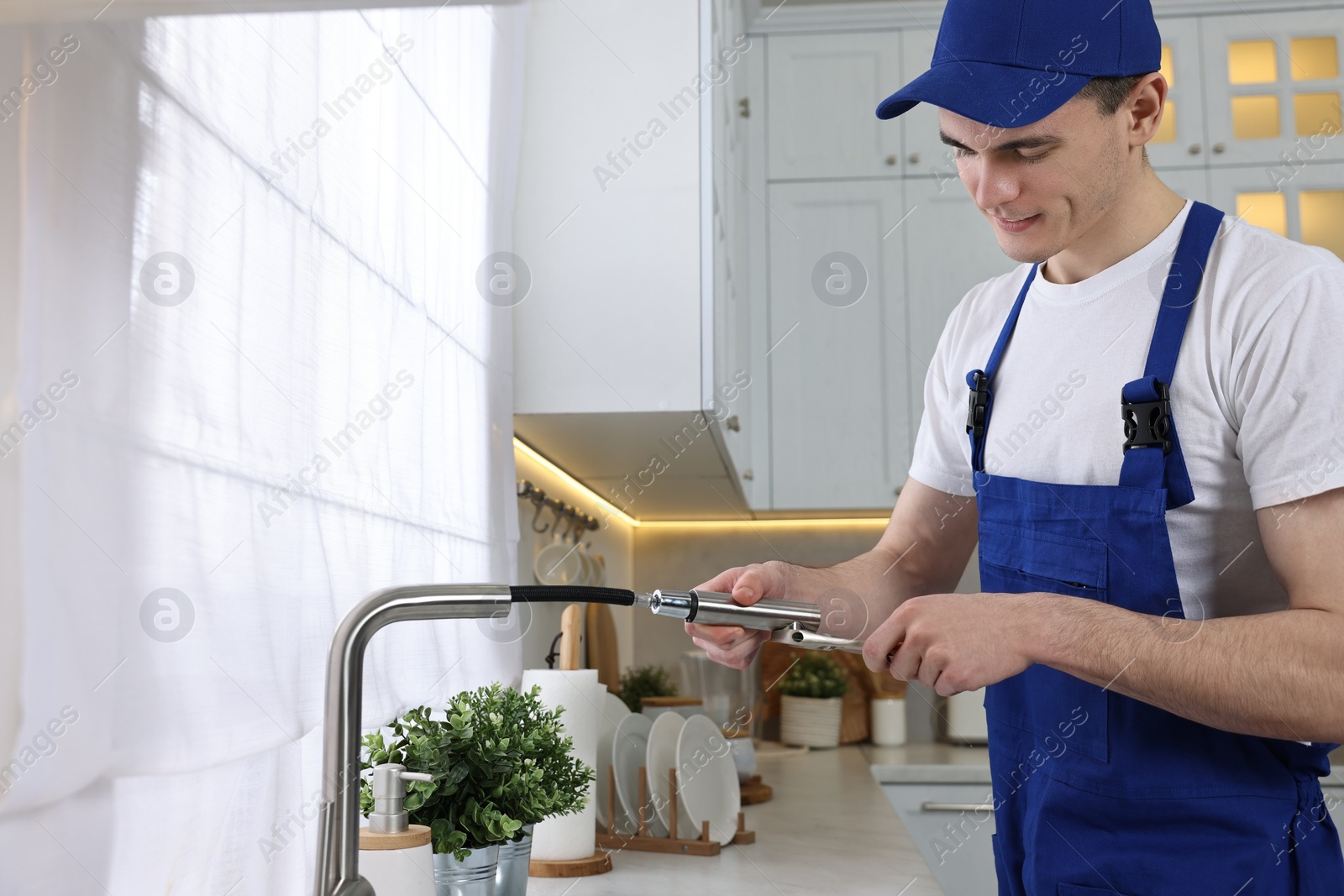 Photo of Young plumber repairing faucet with spanner in kitchen