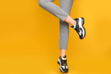 Photo of Woman wearing stylish sneakers on yellow background, closeup. Space for text