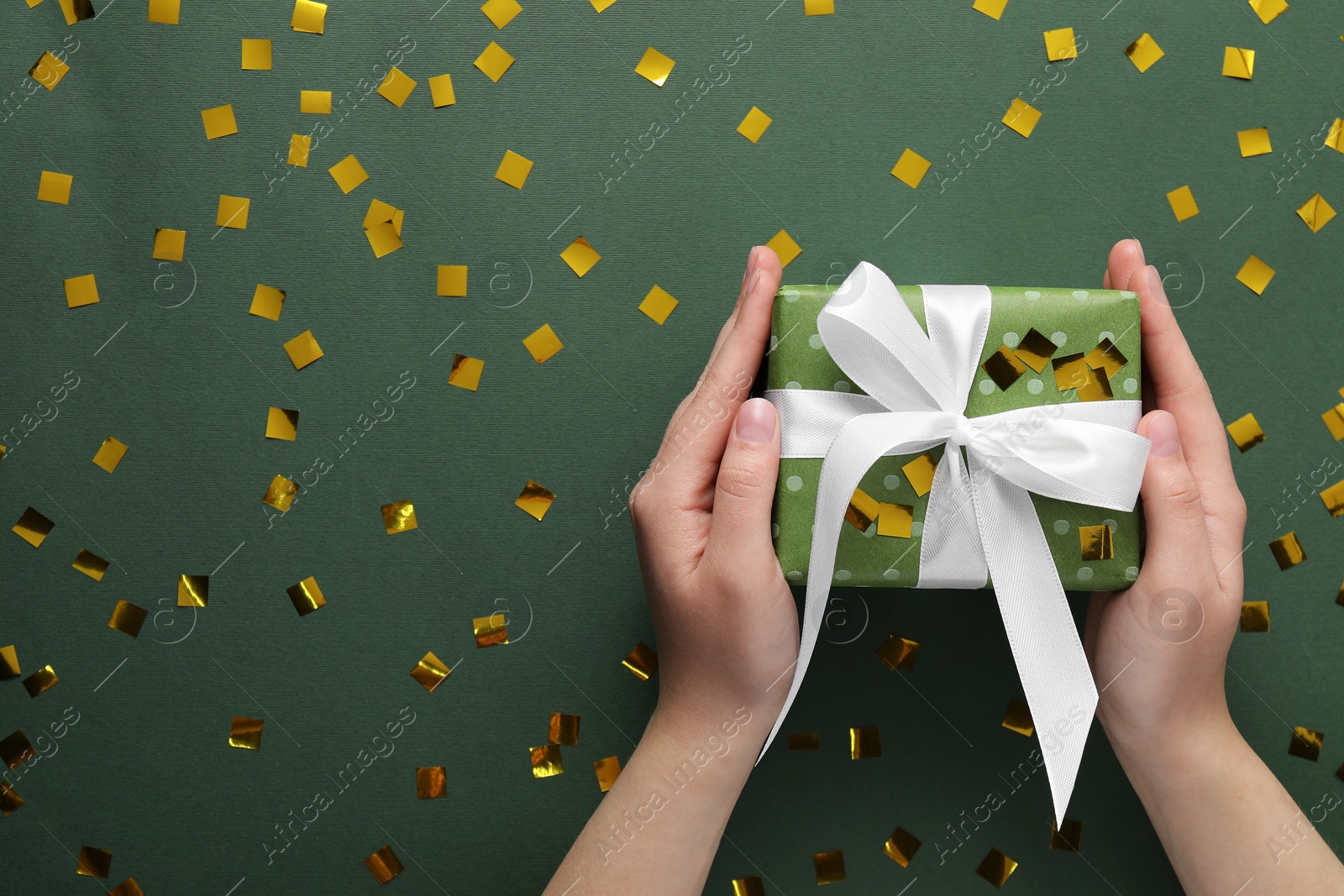 Photo of Woman with Christmas gift and confetti on green background, top view