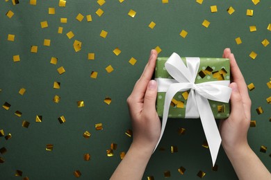 Woman with Christmas gift and confetti on green background, top view