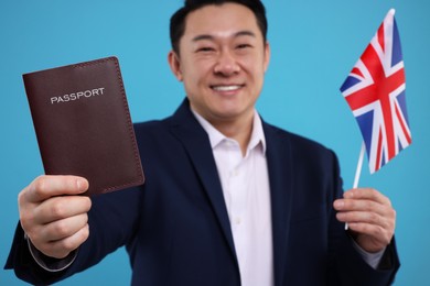 Photo of Immigration. Happy man with passport and flag of United Kingdom on light blue background, selective focus