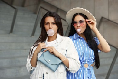 Beautiful stylish women blowing gums near stairs outdoors