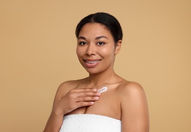Young woman applying cream onto body on beige background
