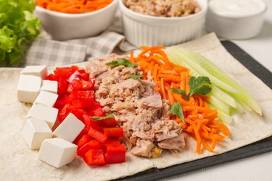 Delicious tortilla with tuna and vegetables on white table, closeup. Cooking shawarma