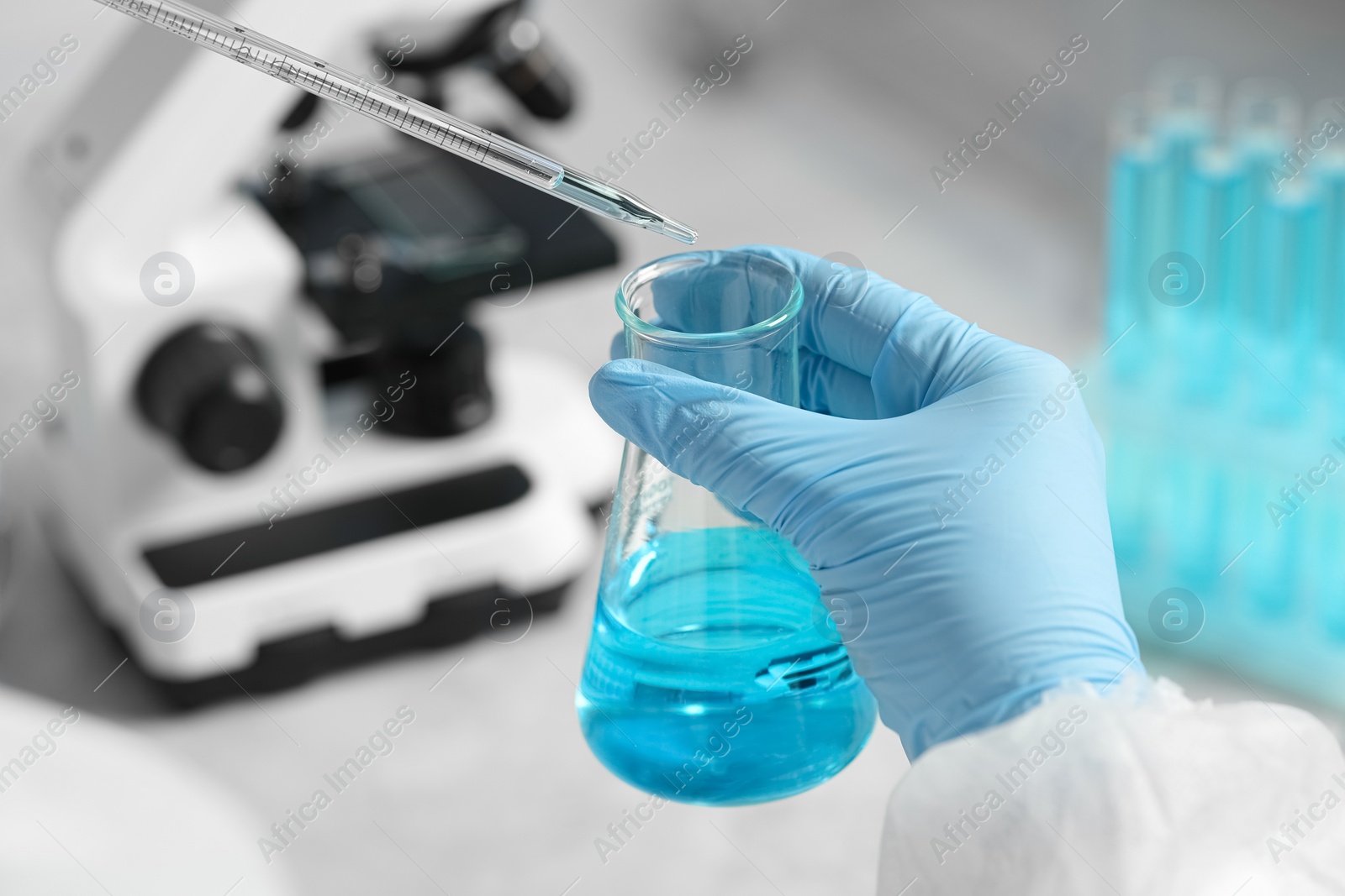 Photo of Scientist dripping liquid from pipette into beaker in laboratory, closeup