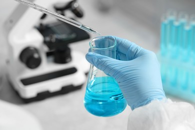 Photo of Scientist dripping liquid from pipette into beaker in laboratory, closeup