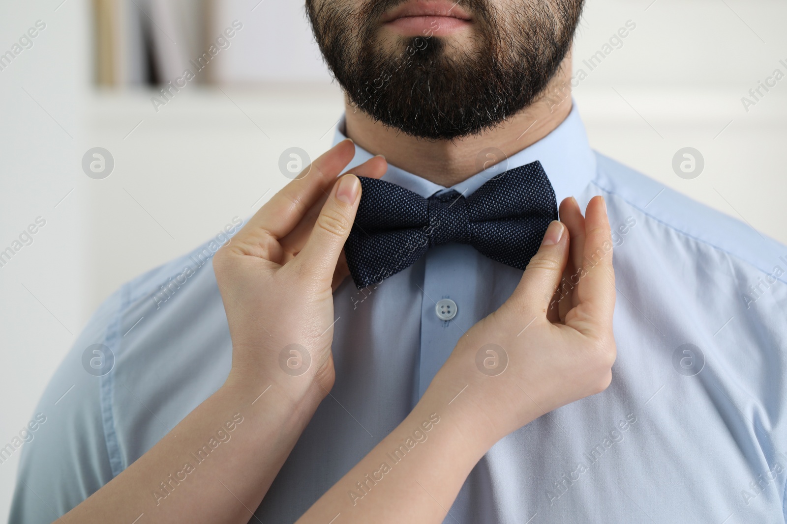 Photo of Woman adjusting bow tie to man indoors, closeup